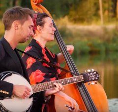 un musicien (banjo) et une musicienne (contrebasse) jouent. Une rivière se trouve à l'arrière plan