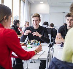 2 Lycéens face à 2 lycéennes de dos, assis autour de tables dans une classes